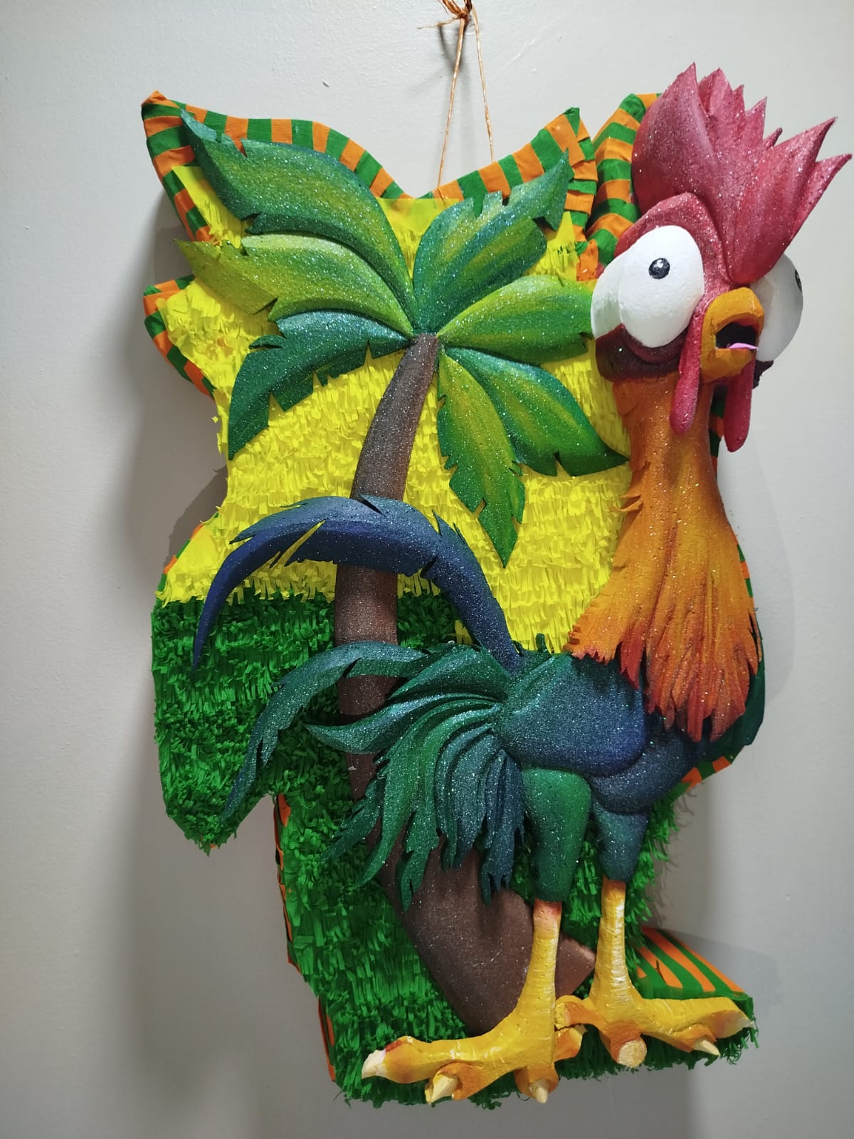 Piñata artesanal de Hei Hei de Moana frente a palmera